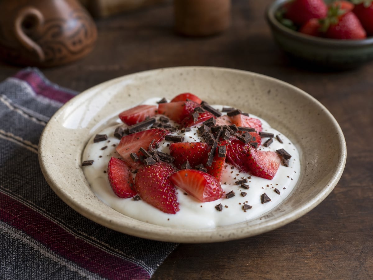 Fresas con yogur y chocolate oscuro servido en una porción casera con ingredientes visibles